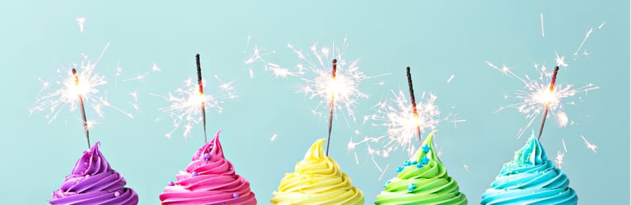 five colorful cupcakes with frosting and sparklers