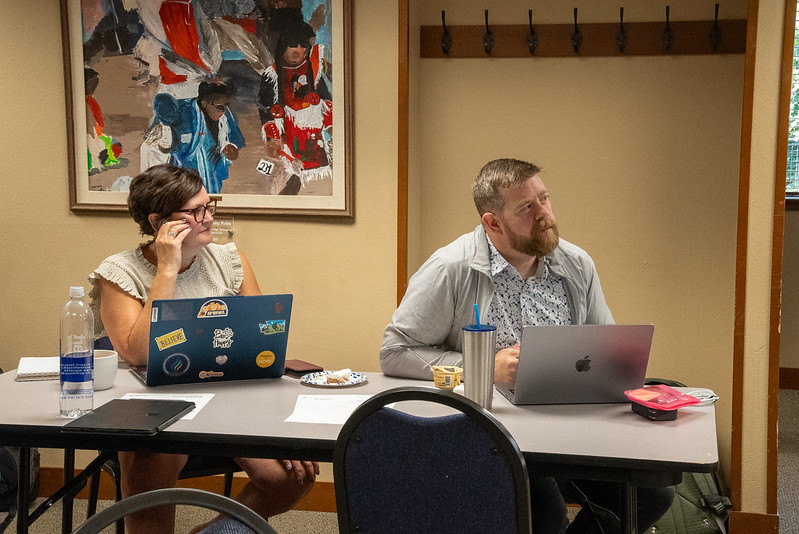 AWSP Staff Man and women sitting at a table looking to the front of the room listening with laptops open.